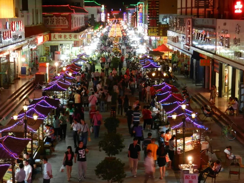 Una veduta notturna di un mercato animato in Cina con molte luci e persone.