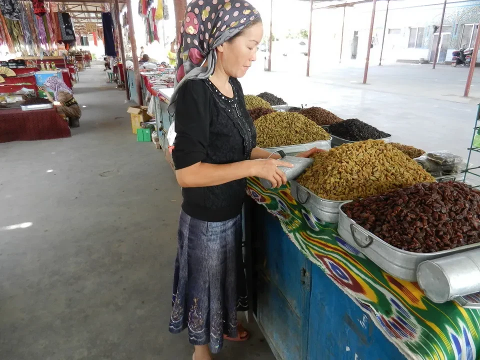 Una donna sta selezionando diverse quantità di frutta secca su un banco in un mercato cinese.