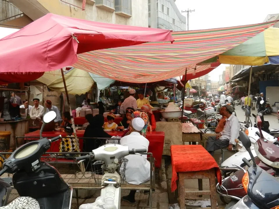 Un mercato animato con venditori e veicoli parcheggiati in una strada cittadina cinese.