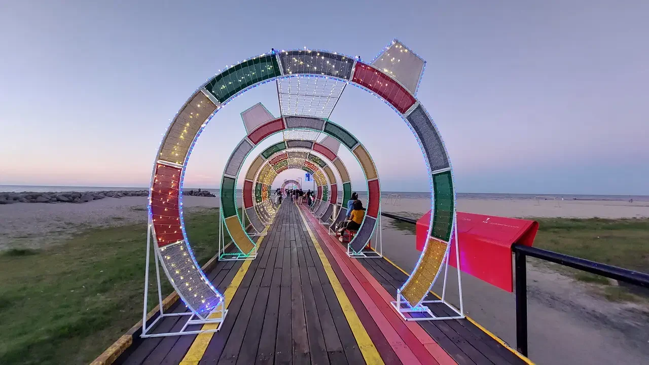 Una passerella decorata con luci si estende verso il mare al tramonto.