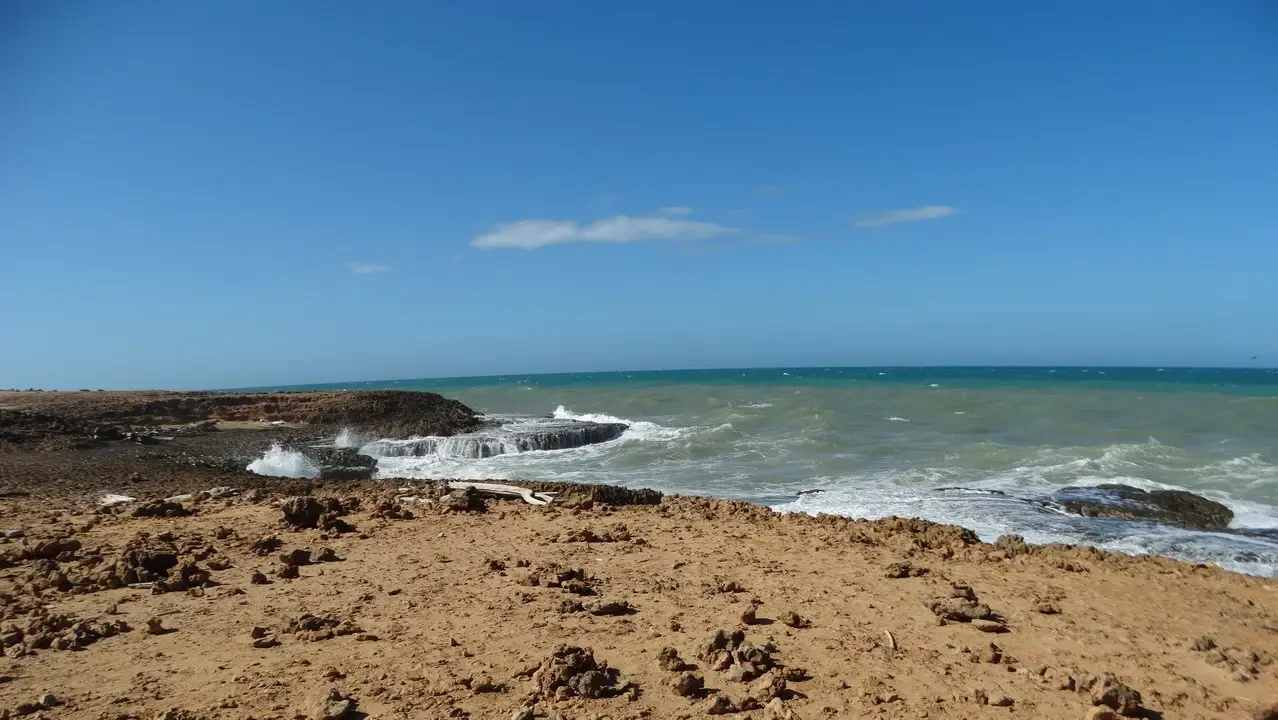 Una spiaggia sabbiosa con onde che si infrangono sulla riva sotto un cielo azzurro.