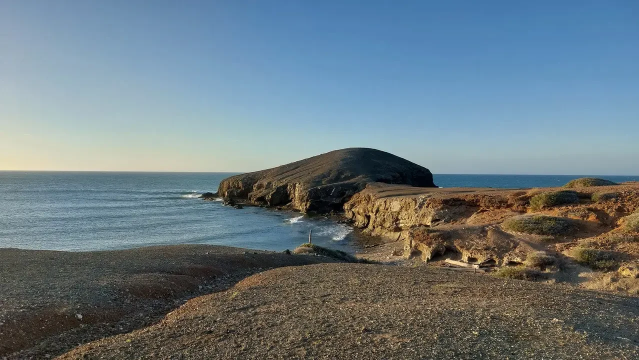 Una formazione rocciosa si protende lungo la costa sotto un cielo limpido.