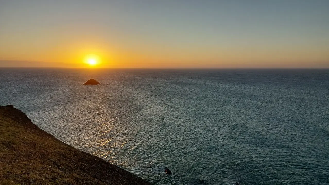 Tramonto dorato sul mare con un'isola rocciosa in lontananza.