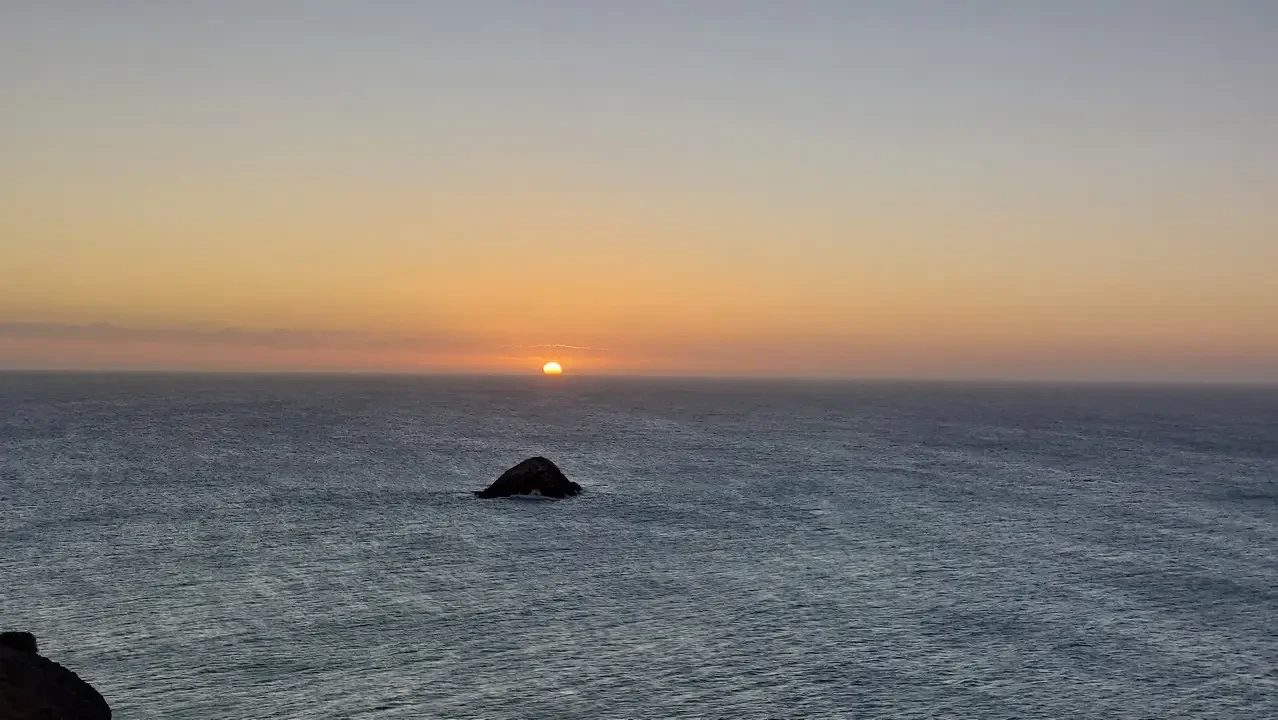 Paesaggio marino al tramonto con un'isola rocciosa nell'acqua calma.