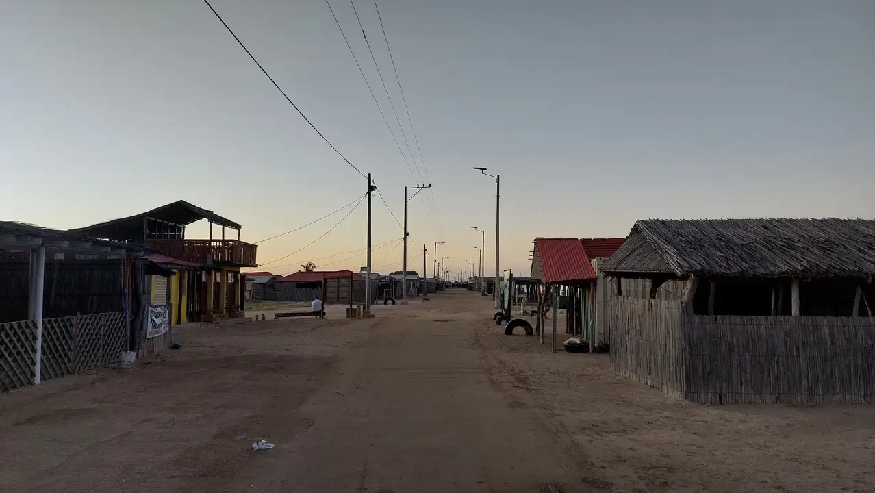 Un villaggio in Alta Guajira, Colombia, mostra case semplici lungo una strada sterrata al tramonto.