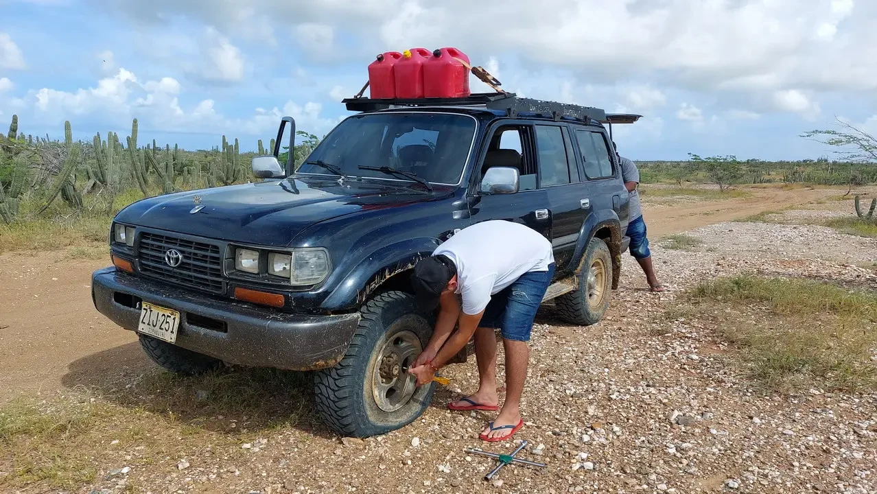 Un uomo si china per lavorare sul tetto di un fuoristrada in un paesaggio arido colombiano.