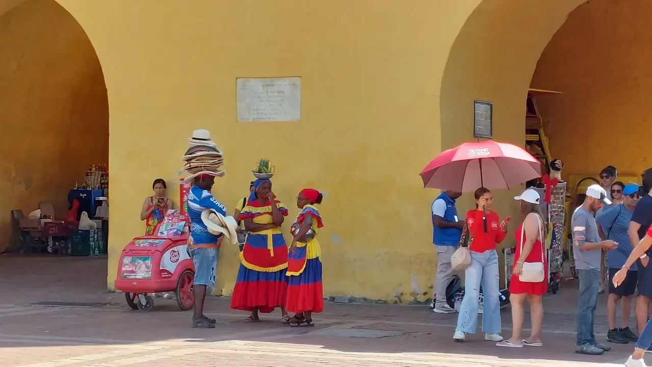 Persone in abiti colorati passeggiano lungo una strada con archi gialli a Cartagena, Colombia.