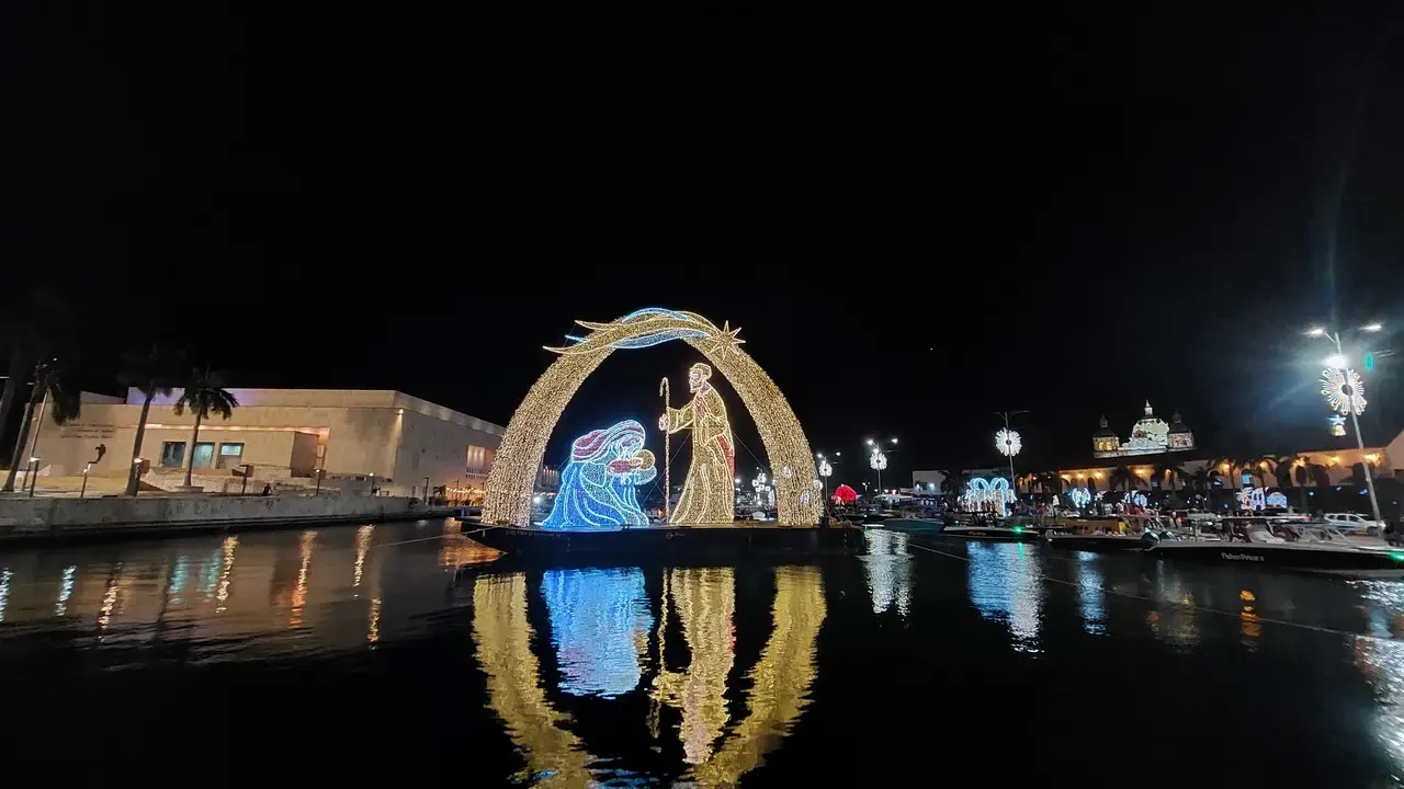 Una nave decorata e illuminata galleggia su un fiume di notte con riflessi sull'acqua.
