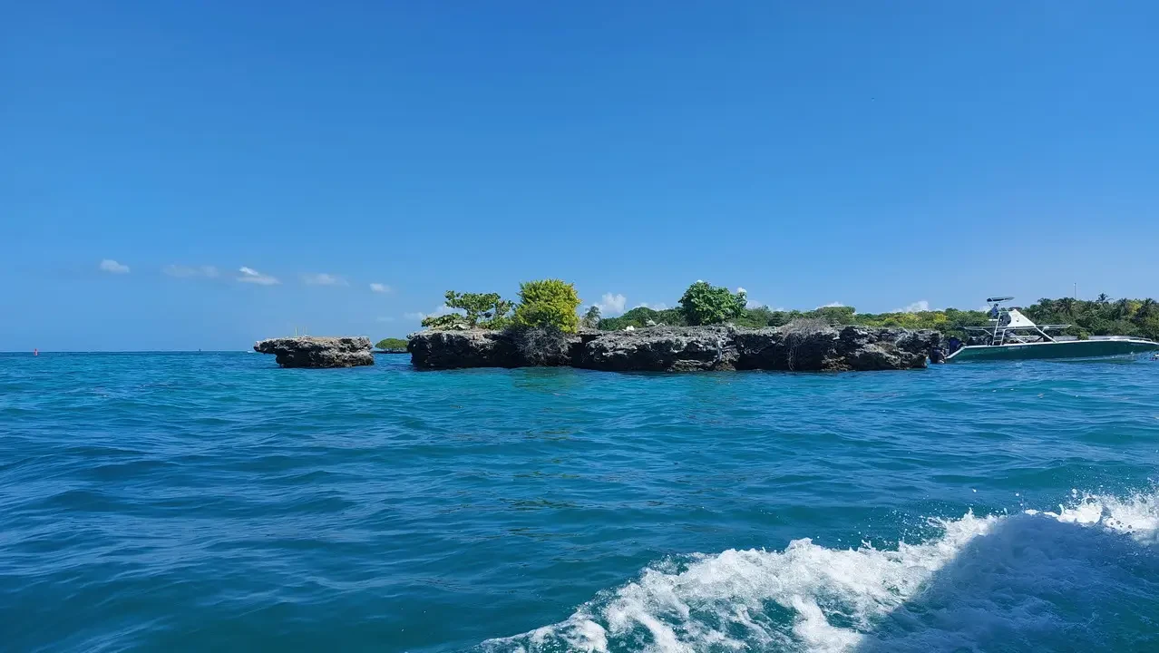 Un'imbarcazione naviga attraverso acque turchesi circondate da scogli rocciosi e vegetazione lussureggiante.