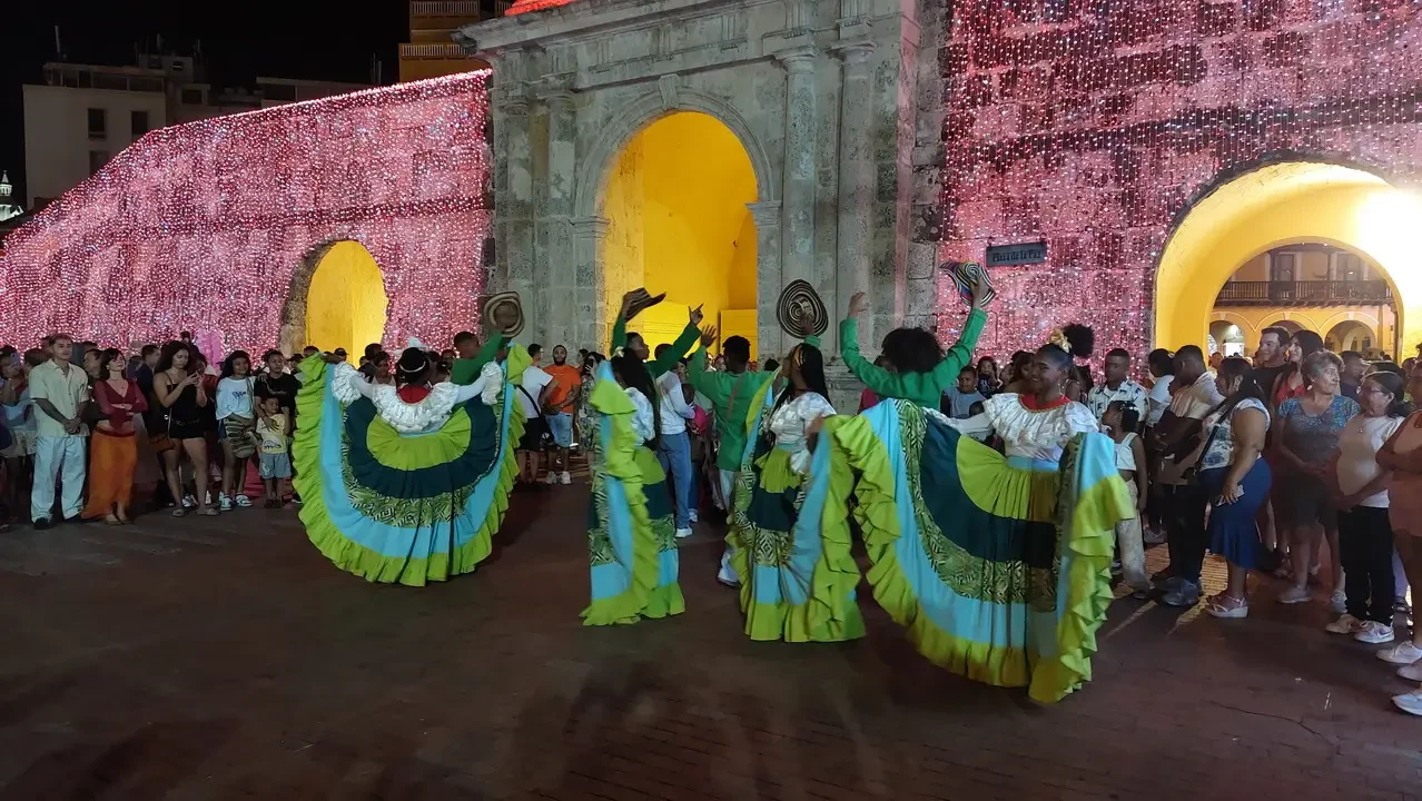 Un gruppo di persone indossa costumi colorati davanti a un arco storico illuminato.