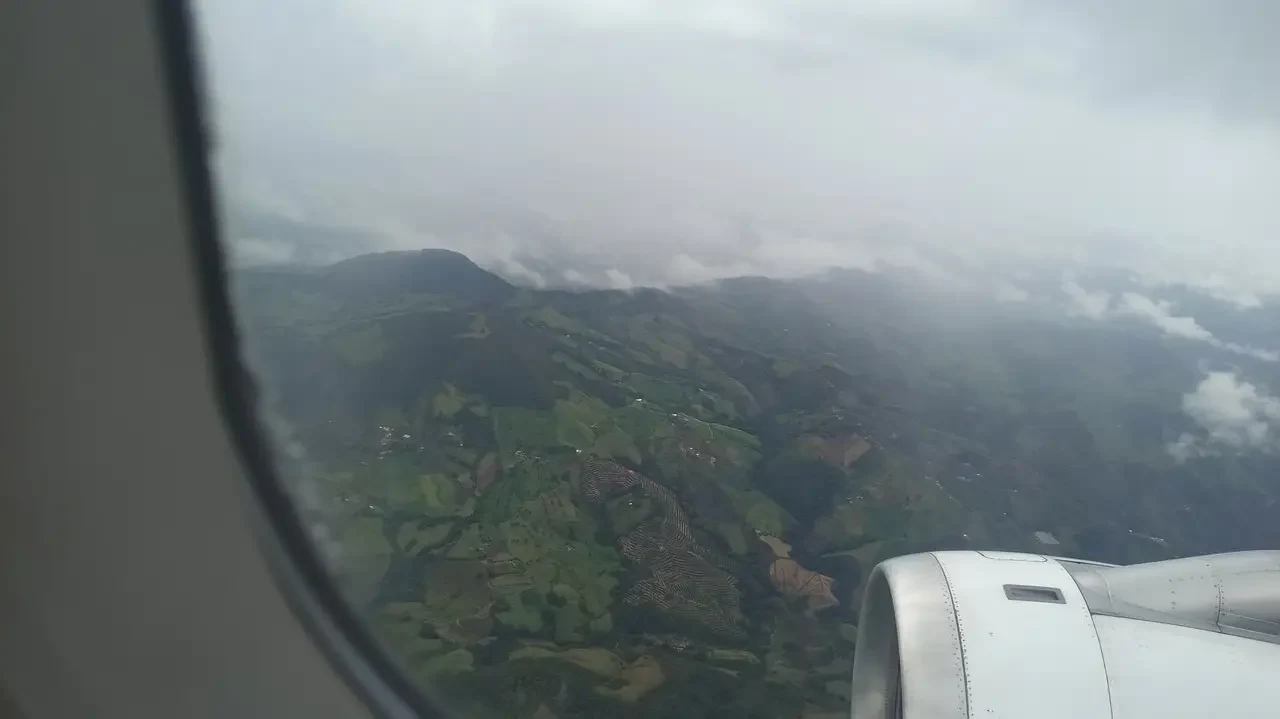 Paesaggio collinare verde e nuvoloso visto dalla finestra di un aereo in Colombia.