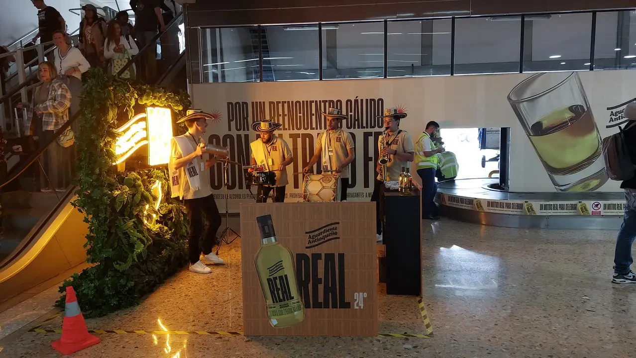 Persone in uniforme e decorazioni posano davanti a esposizioni di bevande all'aeroporto di Medellín.