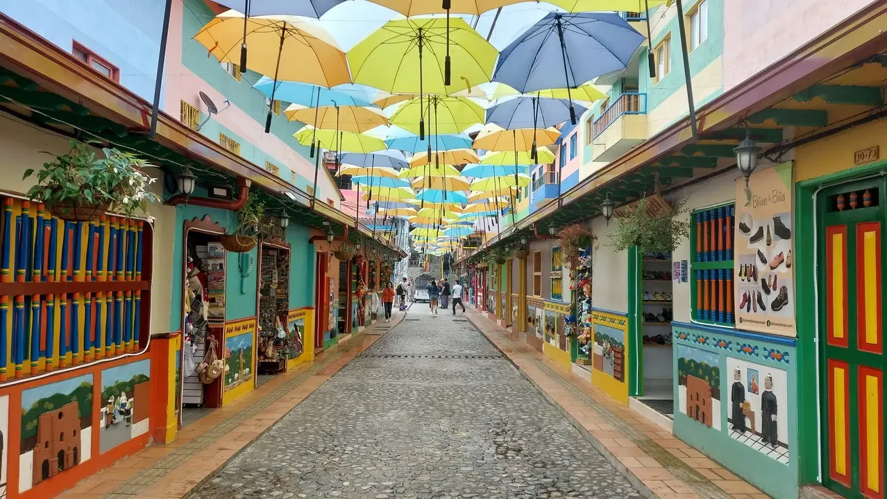 Una strada stretta fiancheggiata da edifici colorati e ombreggiata da ombrelloni vivaci.
