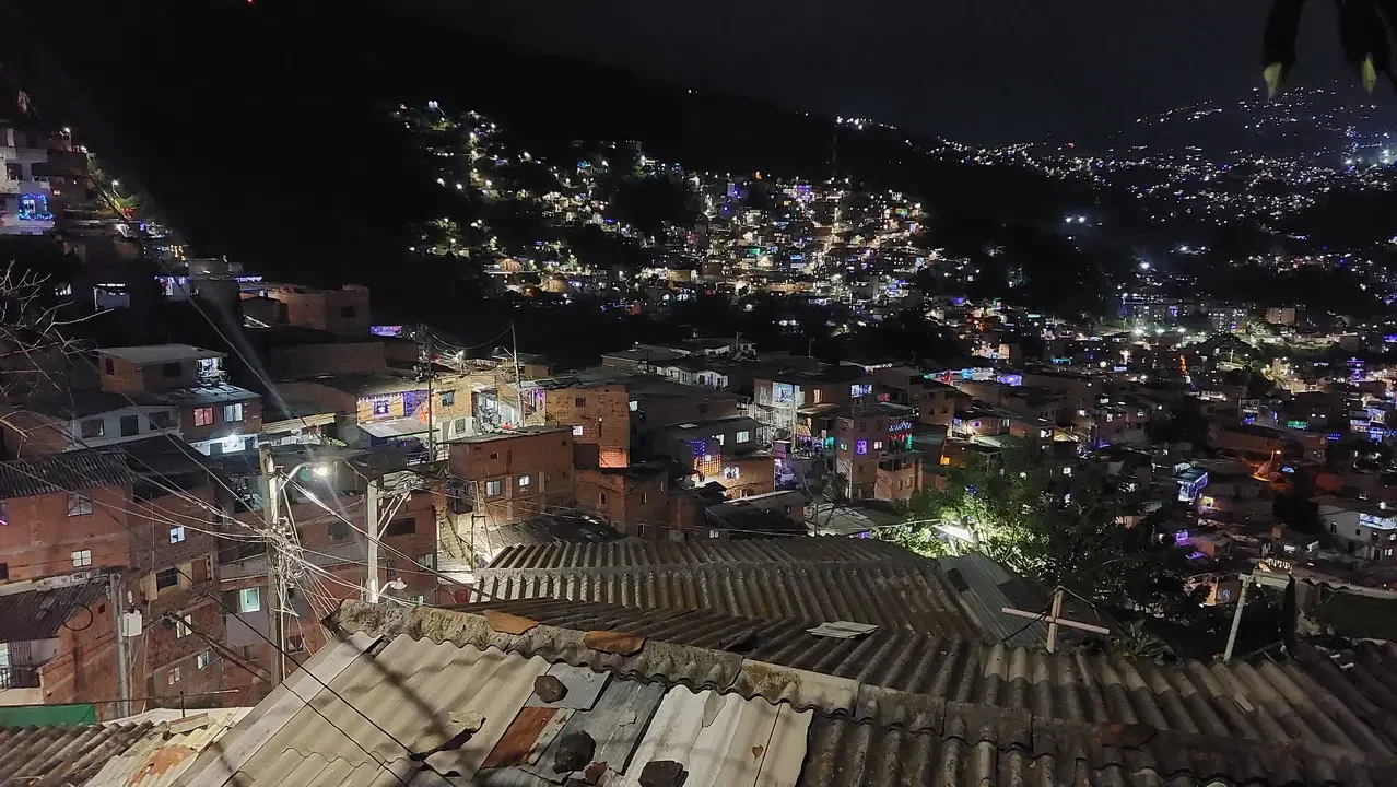 Vista notturna di un quartiere collinare a Medellín con molte luci accese.