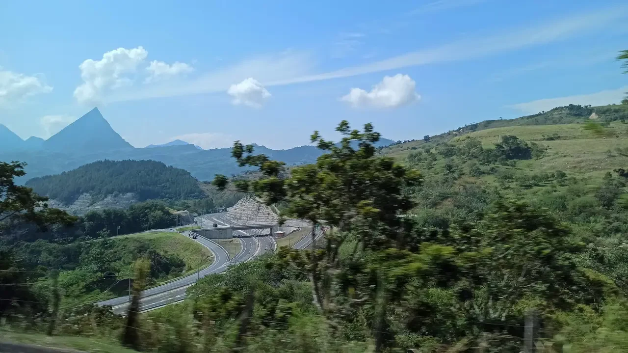 Una strada serpeggia attraverso un paesaggio collinare colombiano con montagne sullo sfondo.