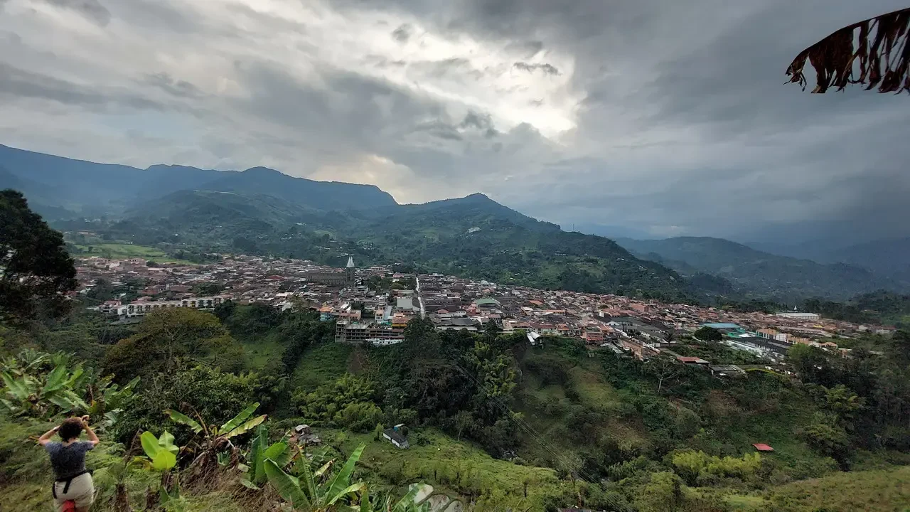Vista panoramica di una città incastonata tra le colline colombiane sotto un cielo nuvoloso.
