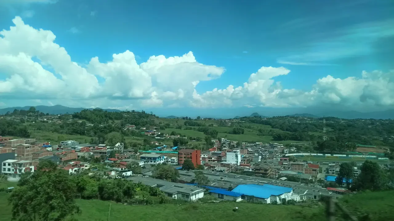 Vista panoramica di un paesaggio urbano e collinare in Colombia sotto un cielo nuvoloso.