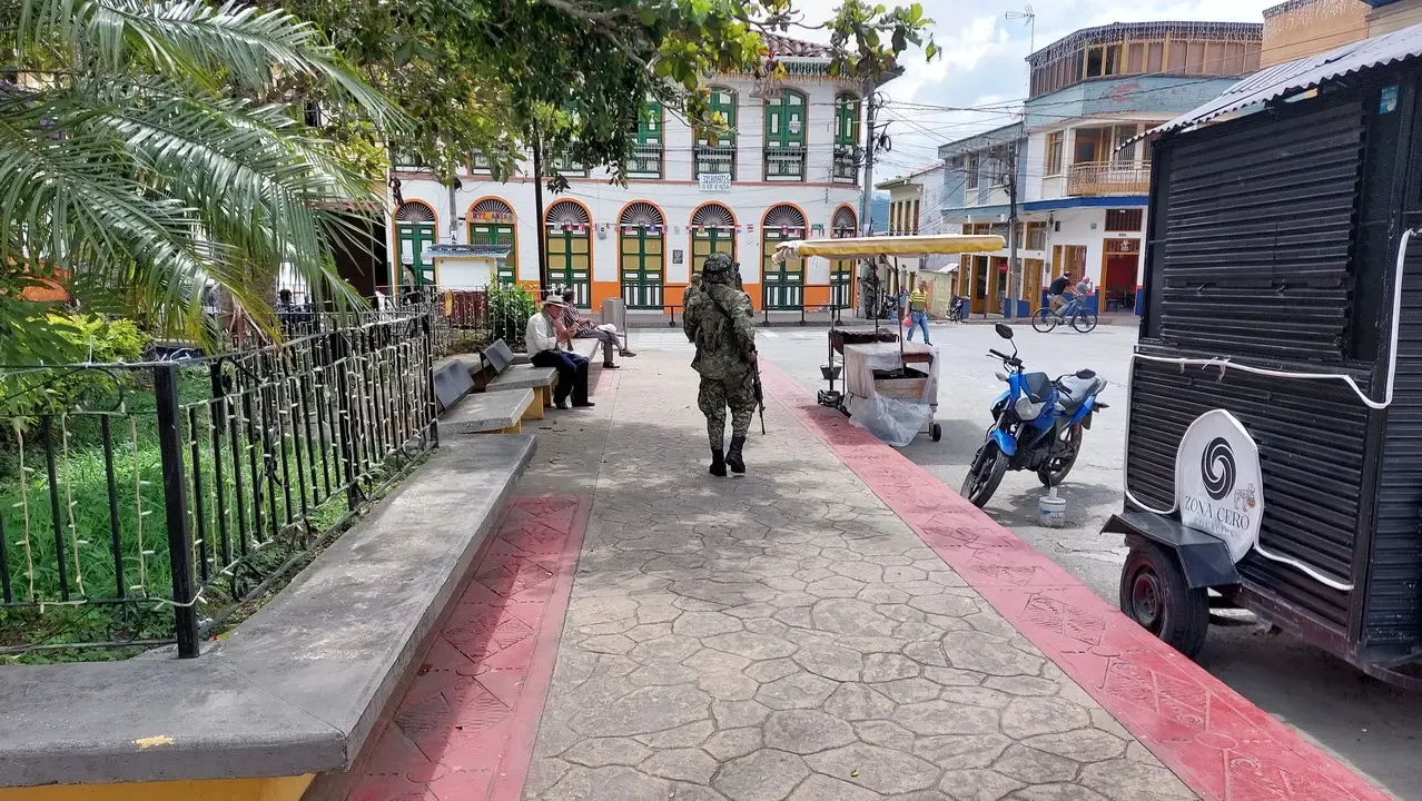 A man in uniform walks along a pedestrian street with colorful buildings in Colombia.
