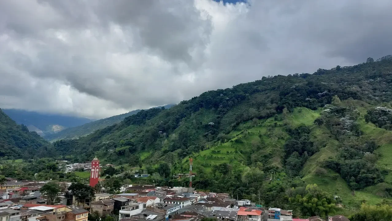 Paesaggio collinare colombiano con edifici in primo piano sotto un cielo nuvoloso.