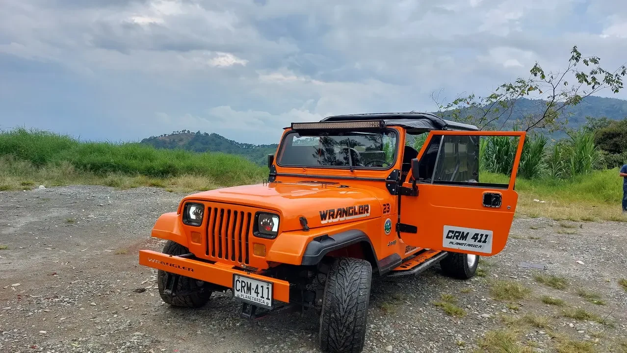 Un veicolo Wrangler arancione è parcheggiato su un terreno accidentato con vegetazione lussureggiante in Colombia.