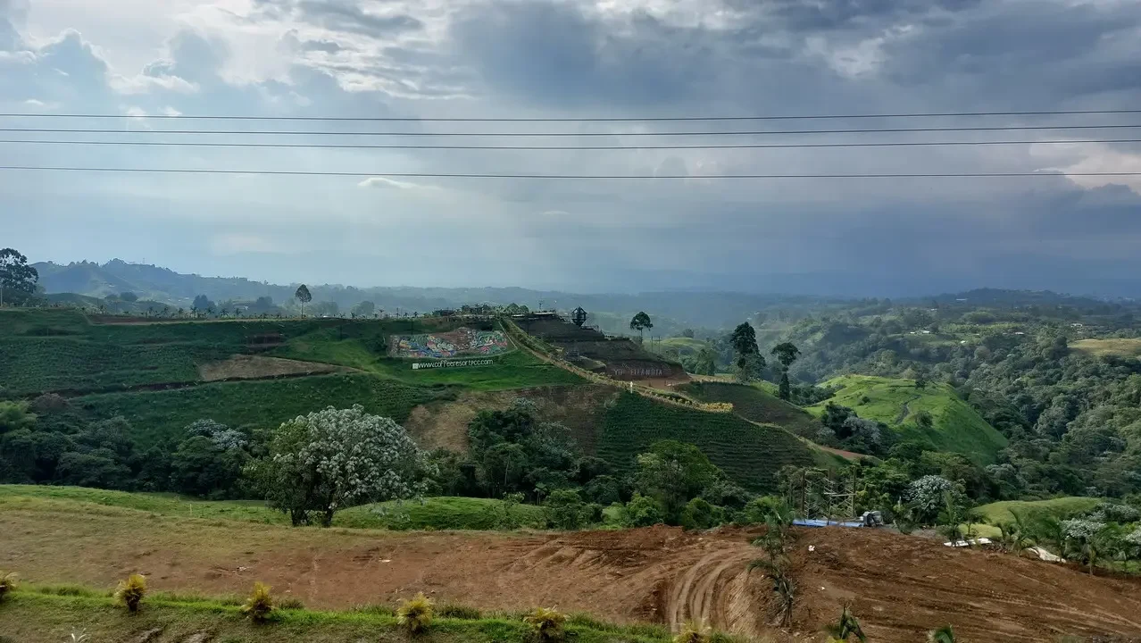 Paesaggio collinare colombiano con campi coltivati sotto un cielo nuvoloso.