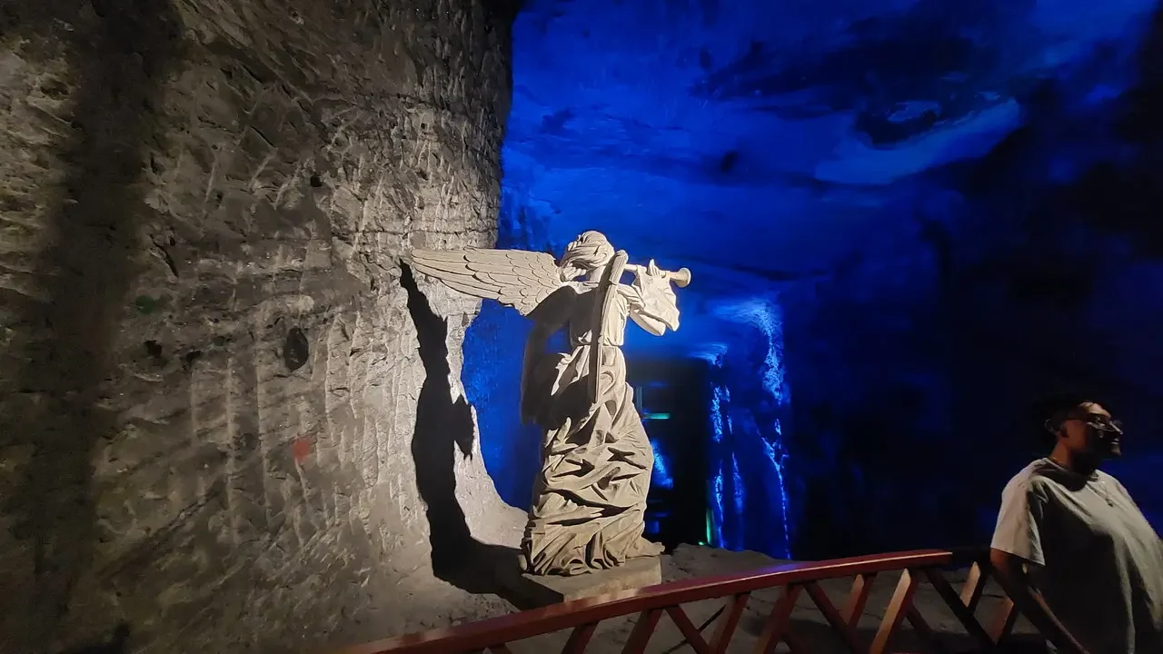 Scultura angelo incastonata nella roccia di una grotta illuminata di blu.