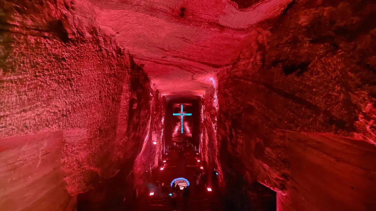 Un lungo corridoio interno rosso conduce a una croce illuminata.