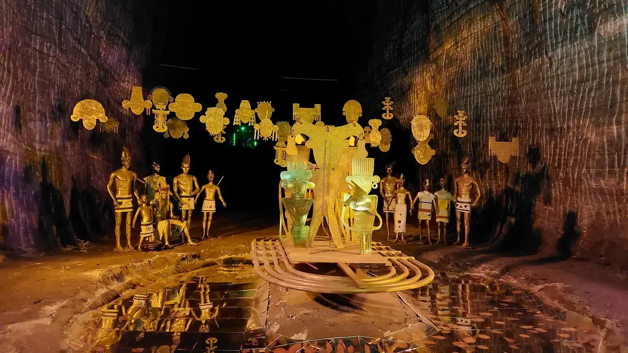 Interno di una grotta illuminato che mostra manufatti dorati e figure stilizzate.