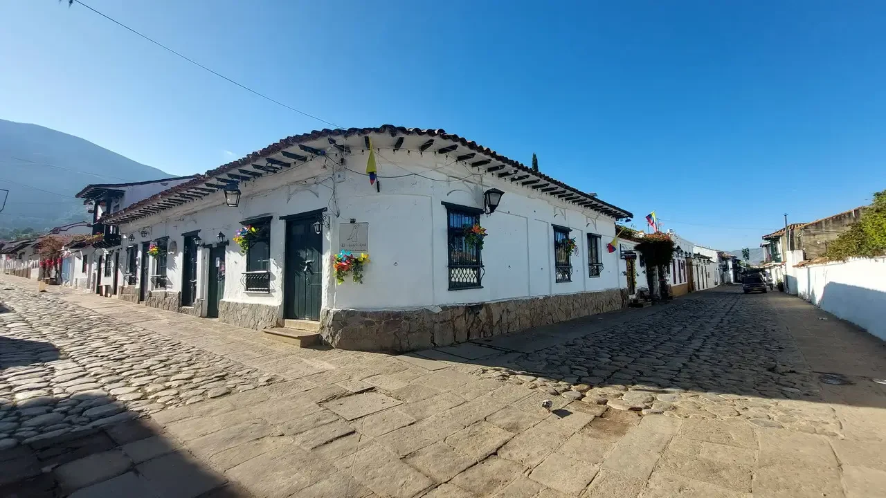 Una strada acciottolata fiancheggiata da edifici bianchi si estende sotto un cielo azzurro in Colombia.