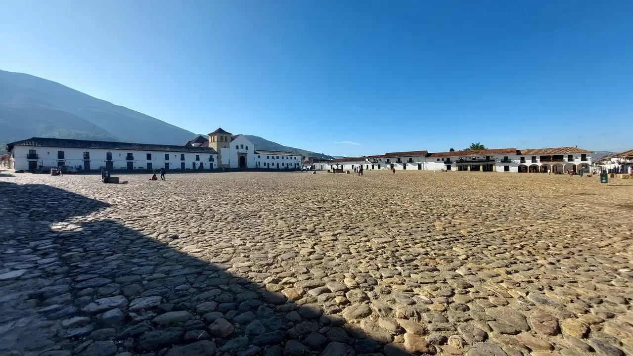 Una piazza aperta con edifici bianchi si estende sotto un cielo azzurro in Colombia.