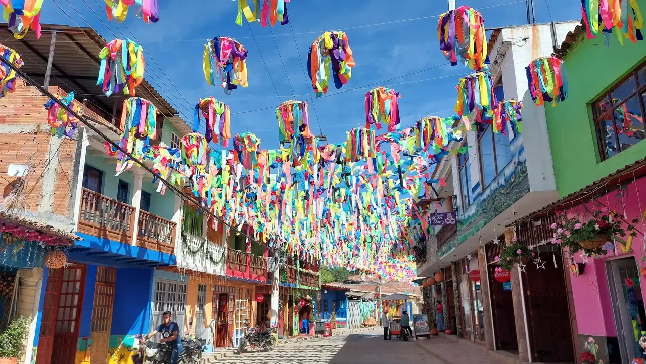 Decorazioni di tessuto colorate pendono sopra una strada fiancheggiata da edifici in Colombia.