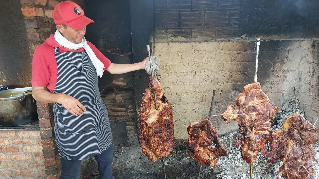 Un uomo arrostisce carne su una griglia all'aperto in un contesto rurale colombiano.