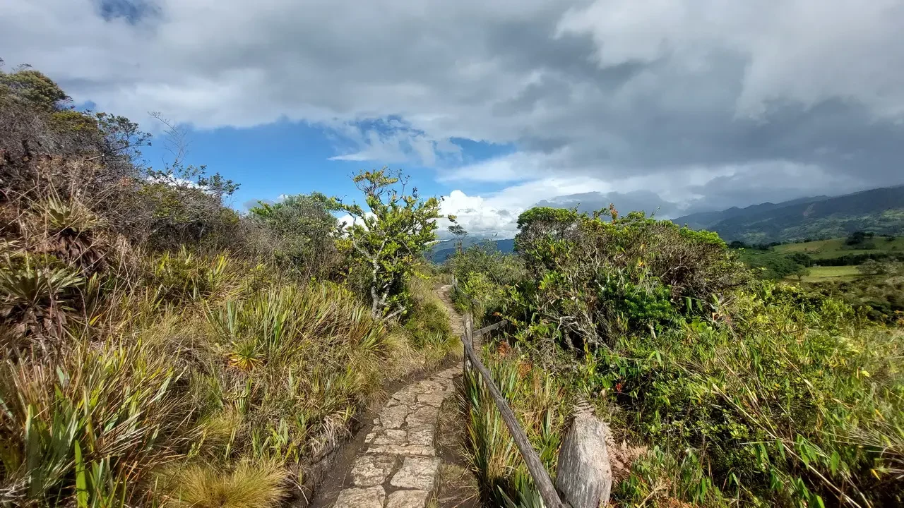 Sentiero sterrato che attraversa un paesaggio montano colombiano sotto un cielo nuvoloso.
