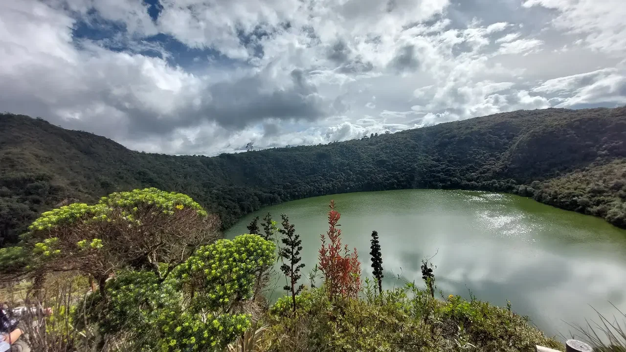 Vista panoramica di un lago circondato da montagne verdi sotto un cielo nuvoloso in Colombia.