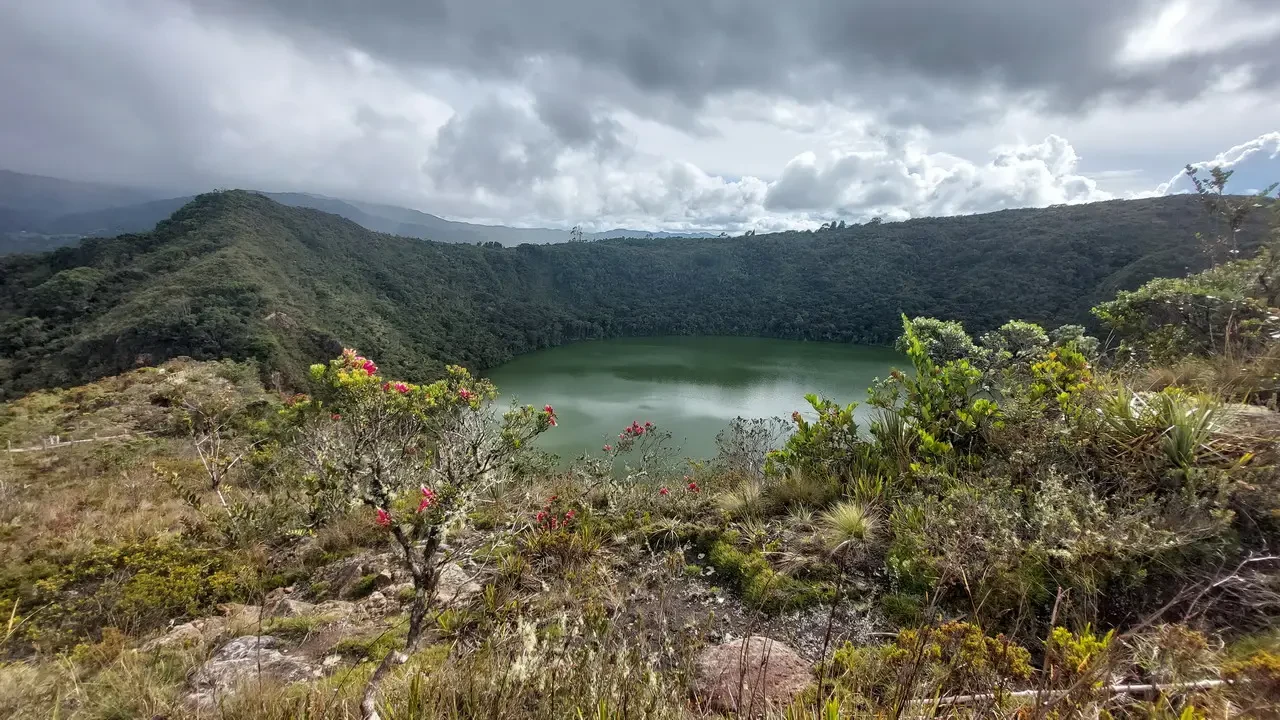 Un lago tranquillo è circondato da colline boscose sotto un cielo nuvoloso.