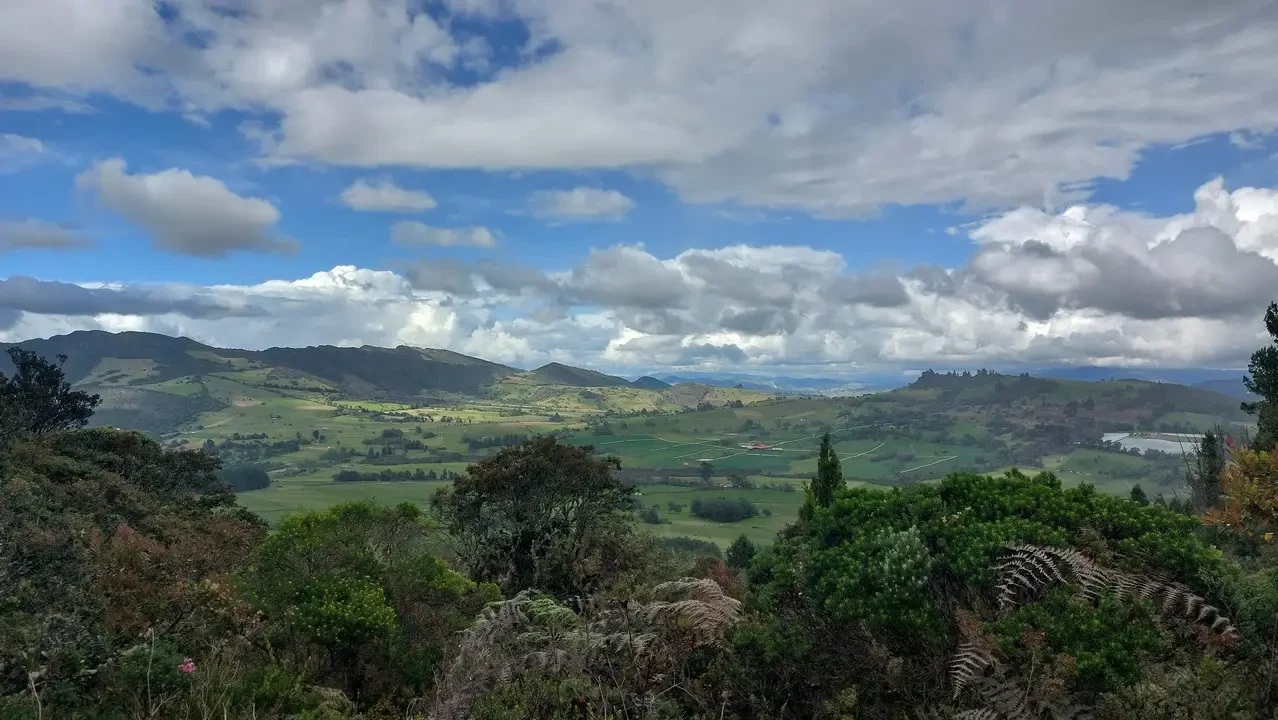 Paesaggio collinare verde con nuvole drammatiche sopra le valli colombiane.
