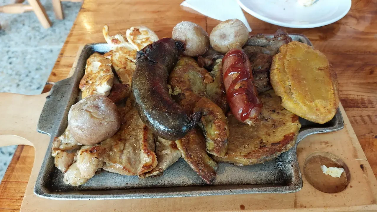 Un piatto di cibo servito su una teglia in legno mostra carni e patate fritte.