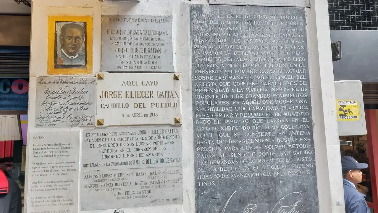 Una fotografia mostra una parete esterna con iscrizioni commemorative in un contesto urbano colombiano.
