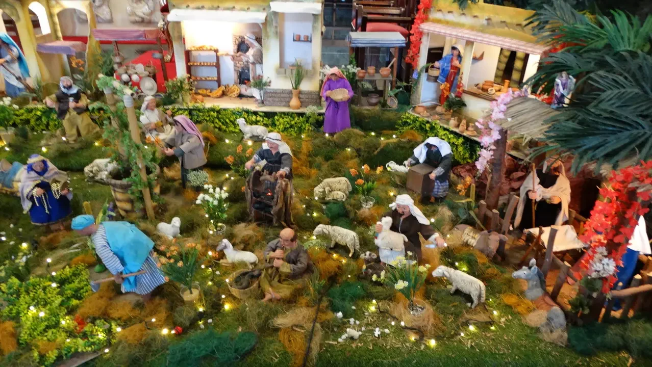Scena di una natività in stile pastorale con figure umane e animali in un paesaggio verde.