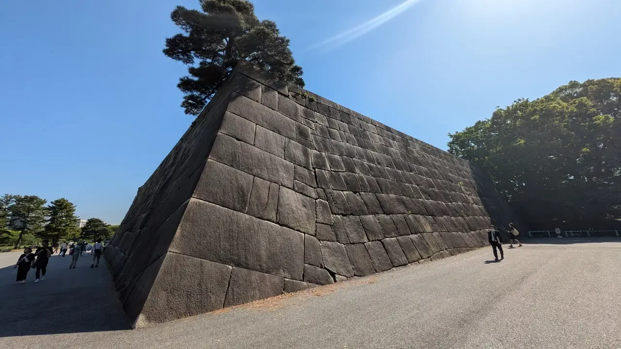 Vista del Palazzo Imperiale di Tokyo con un grande muro di pietra in primo piano.