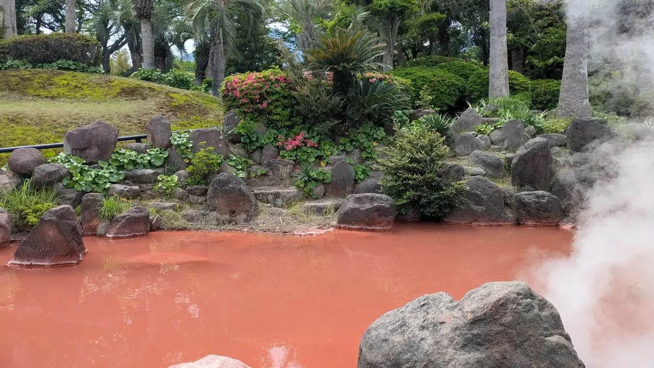 Una sorgente termale rossa con vapore in una zona boscosa giapponese.