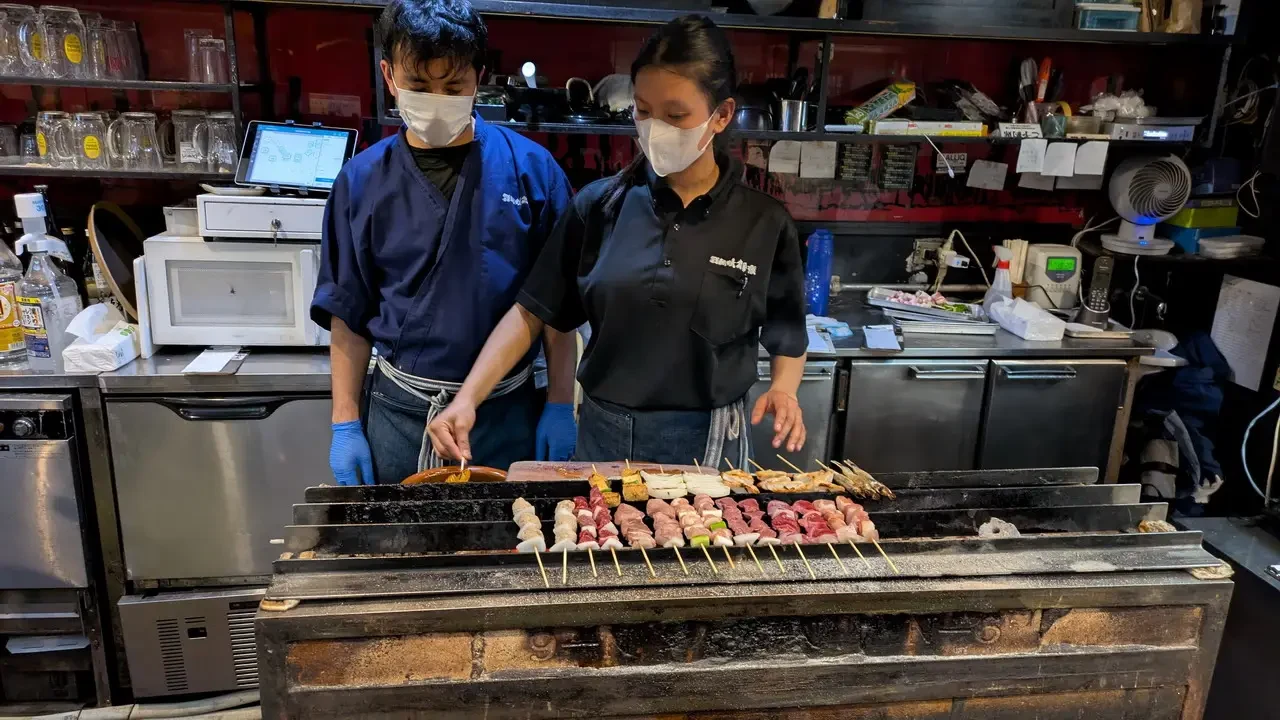 Due cuochi preparano carne su un grill in un ristorante giapponese.