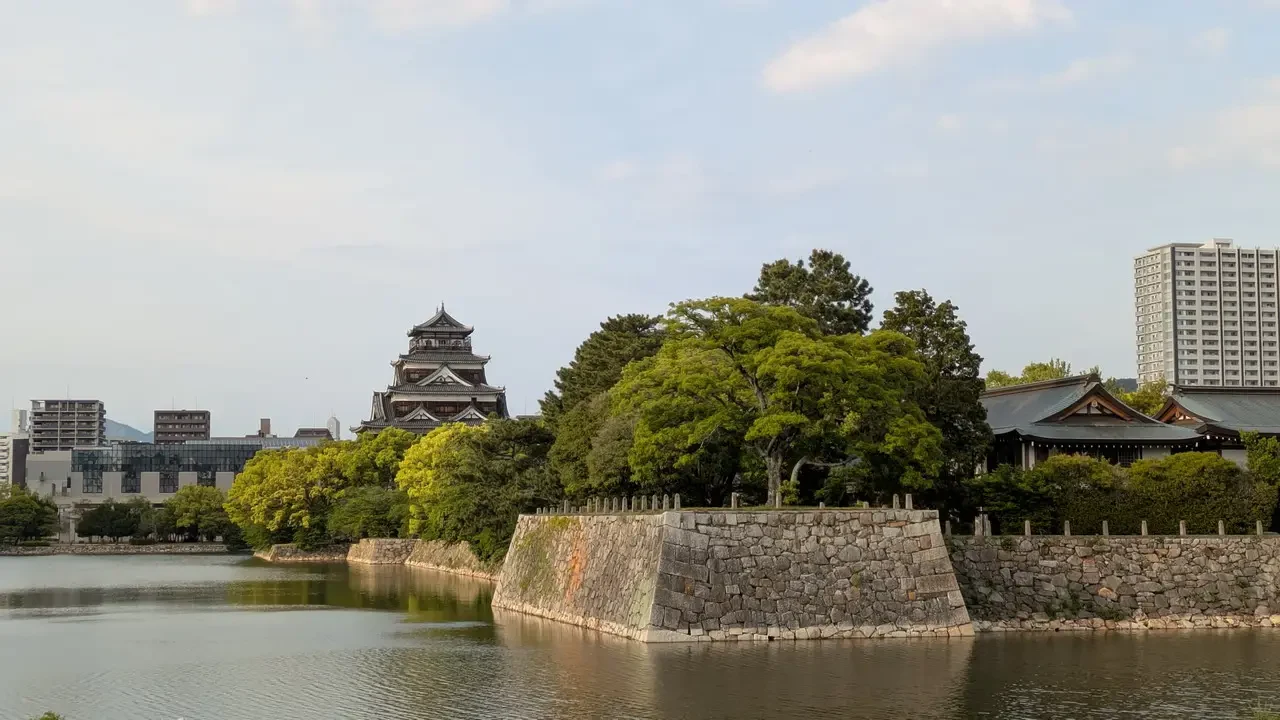 Castello di Hiroshima visibile sull'acqua con vegetazione lussureggiante.