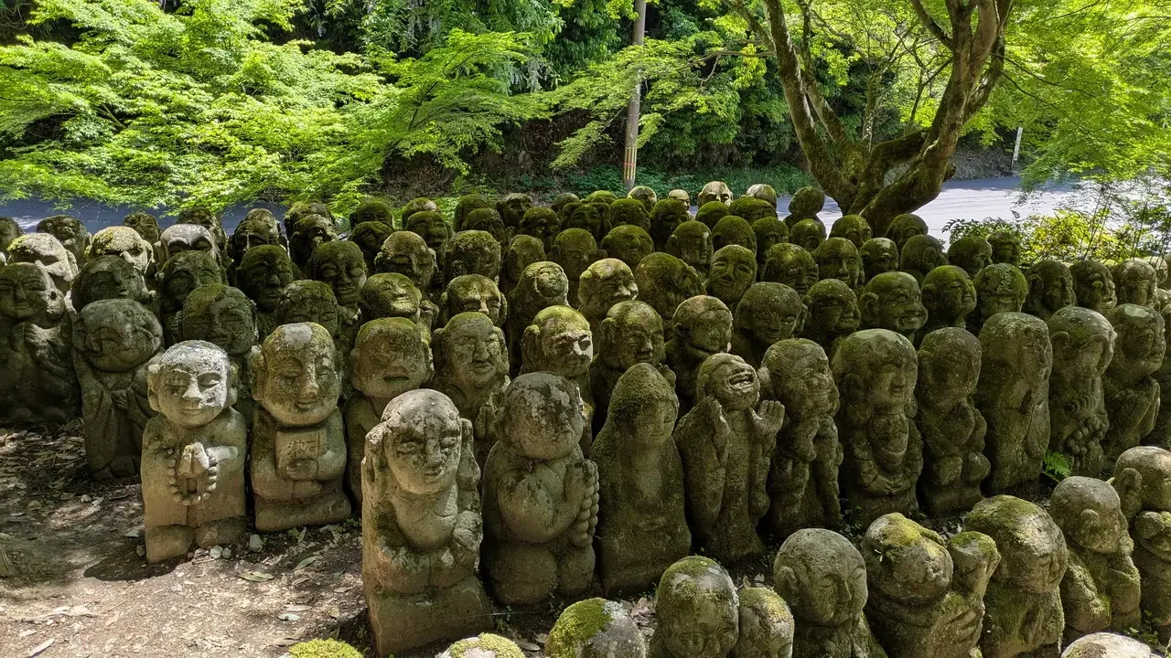 Statue di pietra di Buddha e figure religiose immerse nel verde del giardino giapponese.