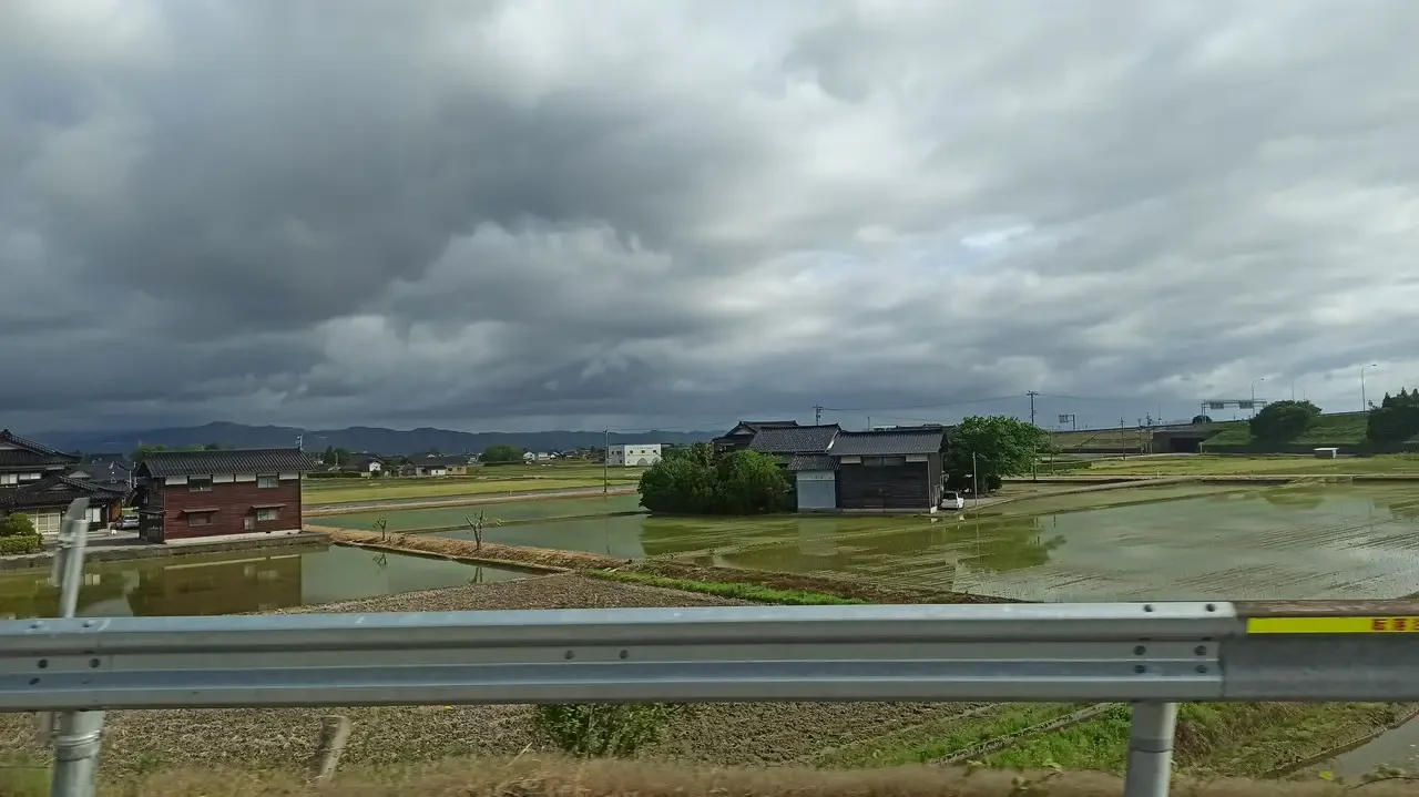 Paesaggio rurale giapponese con edifici tradizionali sotto un cielo nuvoloso.