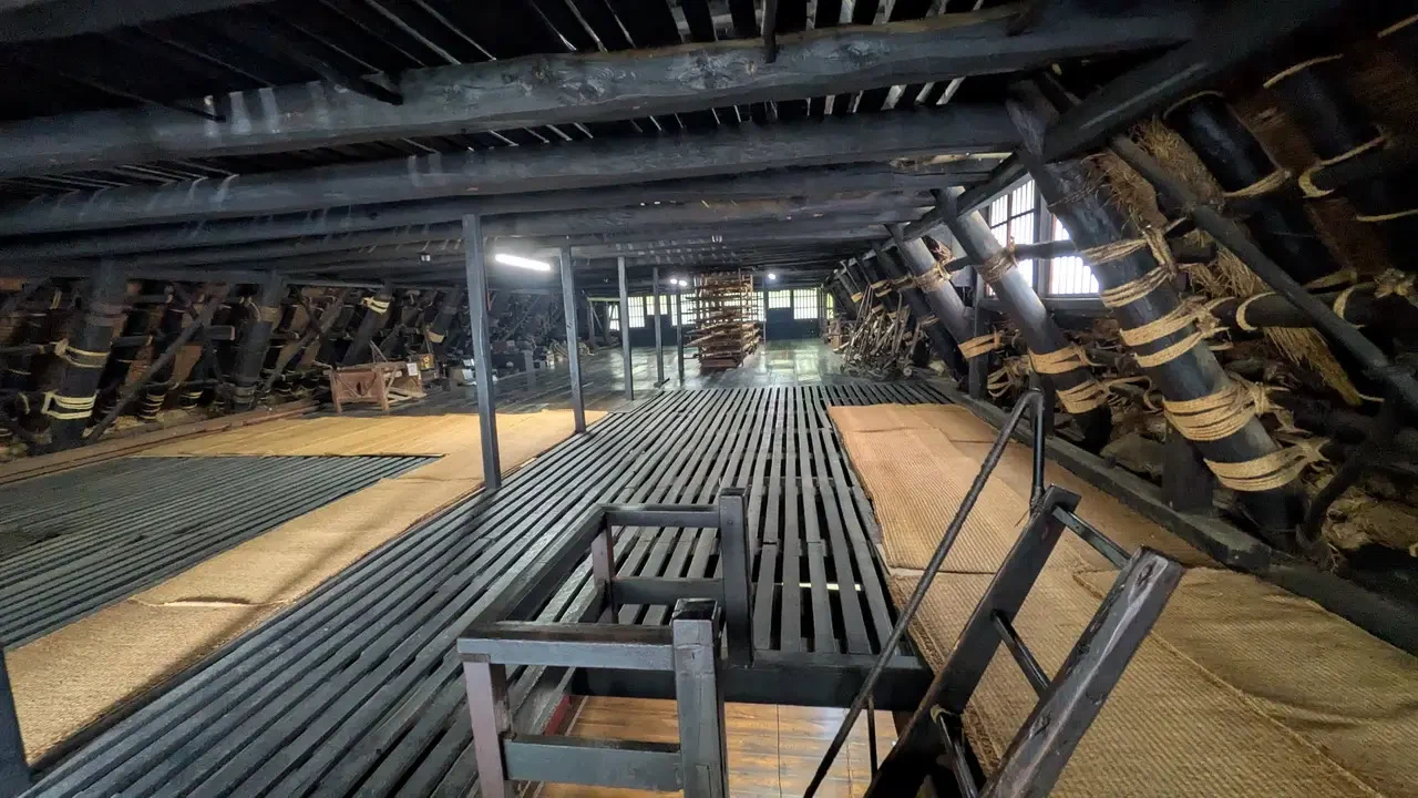 Interno rustico di una struttura tradizionale giapponese con travi in legno esposte.