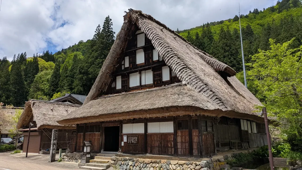 Un tradizionale edificio in stile giapponese con tetto di paglia si trova in una zona boscosa.