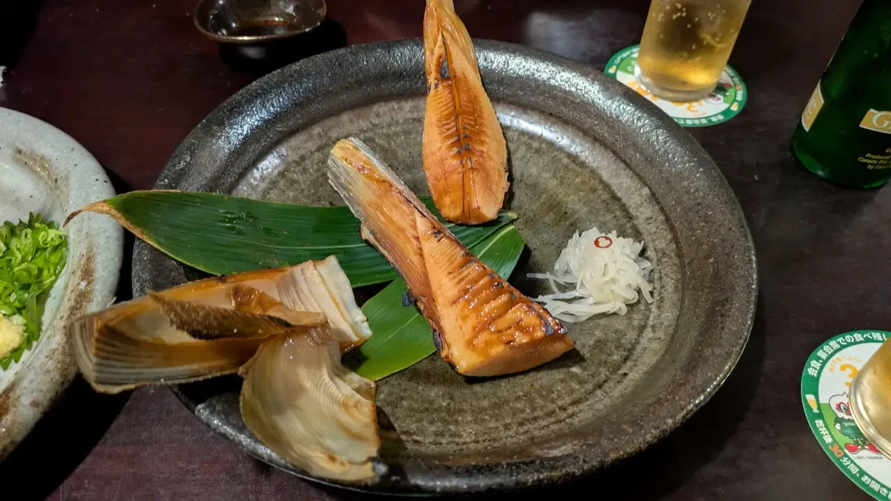 Pesce alla griglia servito su un piatto in stile giapponese con accompagnamenti.