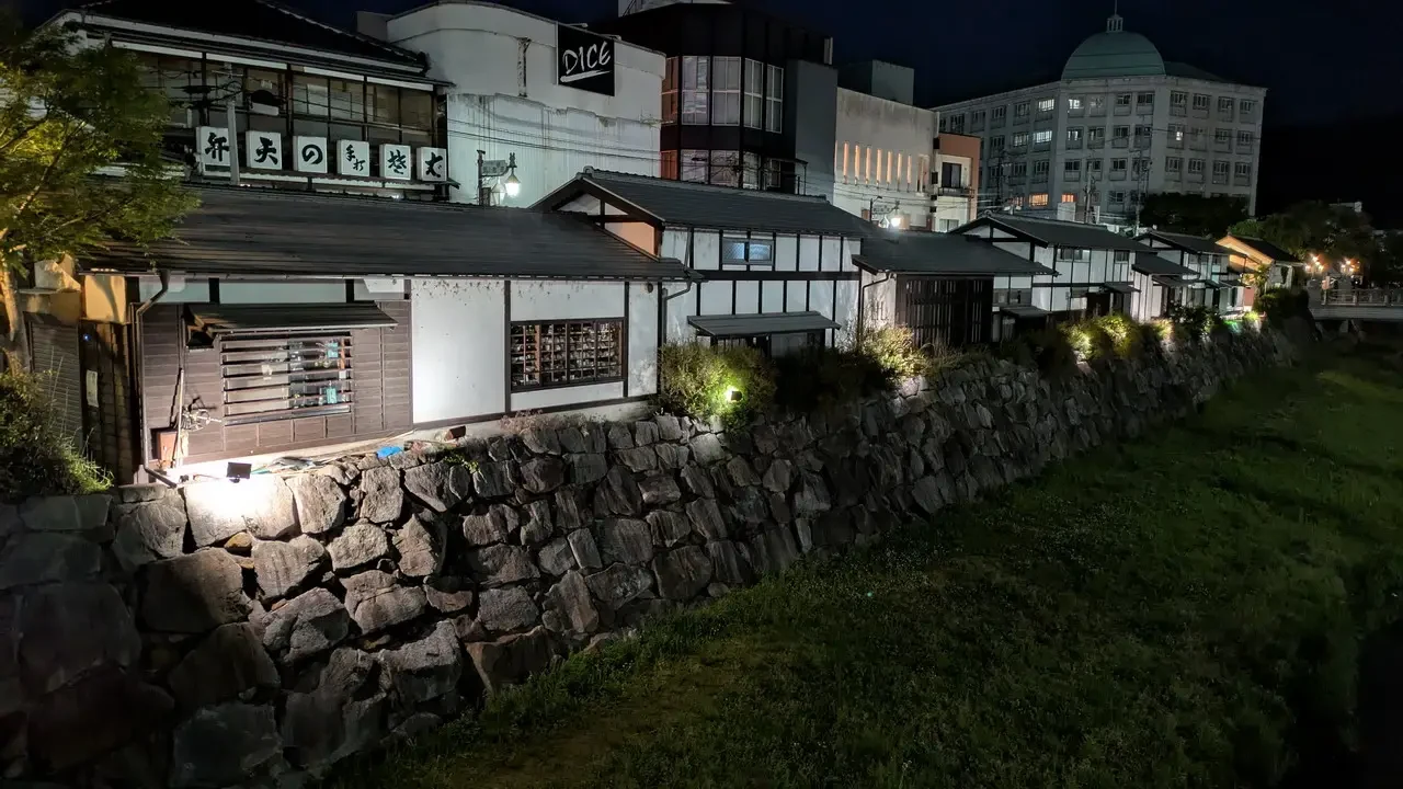 Una fila di edifici tradizionali con tetti in legno lungo un muro di pietra illuminato di notte.