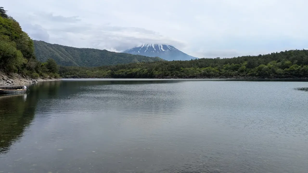 Un lago tranquillo si estende tra colline boscose con una montagna innevata sullo sfondo.